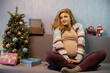 © rubchikova - Pregnant woman is  sitting on the sofa with a gifts near Christmas tree