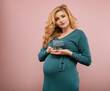 Young pregnant woman with a miniature grocery cart in hands isolated on pink background