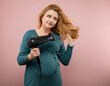 © rubchikova - Beautiful pregnant woman dries her hair with a hairdryer  isolated on pink