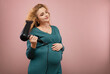 © rubchikova - Beautiful pregnant woman dries her hair with a hairdryer  isolated on pink