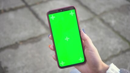 Woman holds mobile phone and swipes photos or pictures outside on a cold autumn day. Use a vertical green screen for copy space closeup. Chroma key mock-up on smartphone in hand. Surfing Internet 4k