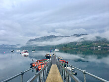 Looking Down The Jetty At Loch Carron After A Rain Storm. Completely Still Water With Misty Cloud, Boats And A Castle In The Background. Plockton, Highlands - Scotland
