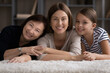 © fizkes - Those closest. Portrait of happy young woman mom daughter lying on floor while old age mommy and preteen child girl hug her from both sides. Loving family dynasty of 3 different females look at camera