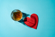 Overhead View Of A Glass Of Whisky Next To A Red Heart On A Blue Background