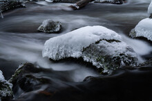 Fast-flowing River Stream With Smooth Water Through The Snow-covered Rocks In The Forest