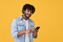 Smiling Indian Young Man Using Cell Phone Isolated On Yellow Background. Happy Guy Holding Smartphone Ordering Online, Making Mobile Banking Payment, Advertising Application On Cellphone.