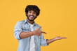 © insta_photos - Excited happy positive young indian man student pointing aside with fingers hand gesture at copy space advertising product, presenting sale discount promo offer standing isolated on yellow background.