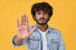 © insta_photos - Serious young indian man showing stop hand objection no gesture sign against forbidden discrimination, violence, expressing refusal, denying rejection or protest isolated on yellow background.