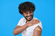 © insta_photos - Happy young adult indian latino man showing bandage plaster on arm after getting vaccination isolated on blue. Vaccine and inoculation, immunization campaign for covid flu prevention concept.