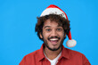 © insta_photos - Excited happy young indian man looking at camera wearing red santa hat advertising Christmas shopping promotion, xmas celebration offers isolated on blue background. Headshot portrait
