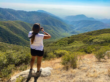Female Standing On The Stone Taking A Picture Of Green Mountains Under A Clear Sky