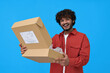 © insta_photos - Happy indian young man holding open parcel box isolated on blue background. Smiling guy customer receiving product retail order purchase in postal shipping delivery unpacking package.