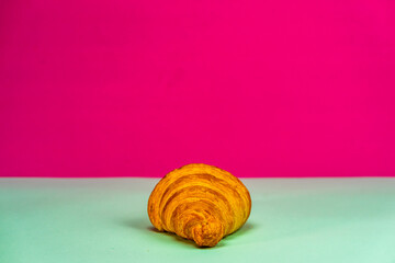 Poster - Closeup shot of a French croissant on a gray surface and pink background