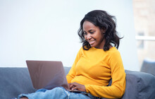 A Young African American Woman Lying On The Sofa While Using Her Laptop At Home