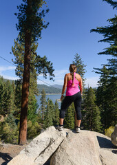 Sticker - Vertical shot of a sporty female standing on the stone looking at the blue lake under a clear sky