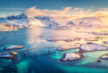 Aerial View Of Bridge, Small Islands, Blue Sea And Snowy Mountains. Lofoten Islands, Norway. Fredvang Bridges At Sunset In Winter. Landscape With Rocks In Snow, Road, Sky, Clouds. Top View From Drone