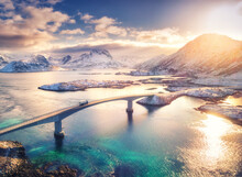 Aerial View Of Bridge, Sea And Snowy Mountains In Lofoten Islands, Norway. Fredvang Bridges At Sunset In Winter. Landscape With Blue Water, Rocks In Snow, Road And Sky With Clouds. Top View From Drone