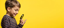 Portrait Of Small Happy Exited Caucasian Boy Curious Child Holding A Magnifying Glass For Reading In Hand Inspecting Or Investigating To Have Close Look Side View - Copy Space Yellow Background