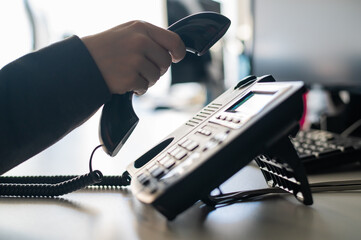 Close-up of the hand of a female office worker dialing a number on a landline phone. Faceless woman secretary calls on the phone