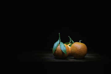 Wall Mural - Closeup of mandarins with leaf Light painting on wooden table and black background