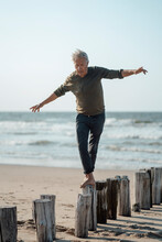 Carefree Senior Man Balancing On Wooden Posts At Beach