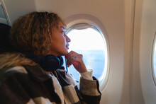 Young Woman With Hand On Chin Looking Out Of Airplane Window