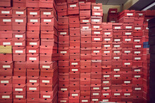 Big Wall Of Lots Of Red Cardboard Package Boxes With Footwear Stacked At A Factory Warehouse. Shoe Manufacturing Industry, Bulk Trade, Distribution And Business Concepts