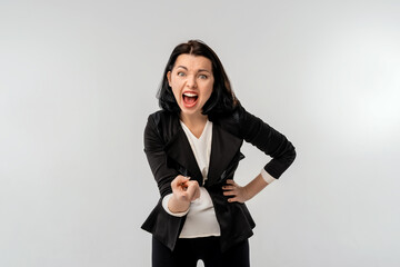 Businesswoman in black formal jacket white shirt pointing at camera with an angry aggressive expression looking like a furious, crazy boss, white background. Business concept