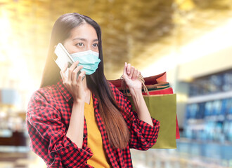 Wall Mural - Asian woman in face mask using a mobile phone while carrying shopping bags