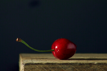 Canvas Print - Selective focus shot of a cherry on a wooden surface with dark background