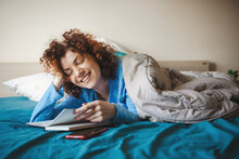 Caucasian Woman Reading Something During Leisure Time In Bedroom. Smiling Face. Coronavirus