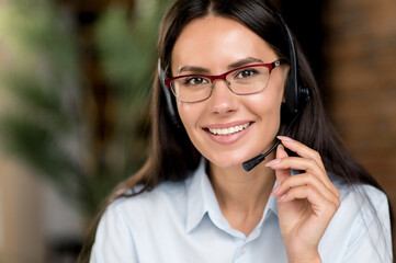 Close up portrait cute joyful caucasian brunette business lady, consultant or top manager, successful real estate agent, wearing glasses and headset, in formal clothes, looking at camera, smiling