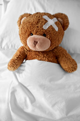 Wall Mural - medicine, healthcare and childhood concept - ill teddy bear toy with medical patch on head lying in bed