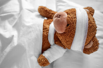 Wall Mural - medicine, healthcare and childhood concept - ill teddy bear toy with bandaged paw and head lying in bed