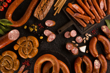 Wall Mural - Sausage and meat delicacies. Sliced ham, sandwiches, german sausages, olives, baguette, nuts, cheese, black bread with spices on a black background. Background image, copy space, flatlay, top view