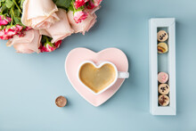 Cup Of Coffee In Shape Of Heart With Chocolate Candies And Bouquet Of Roses On Blue Background. Love Concept.  Top View.