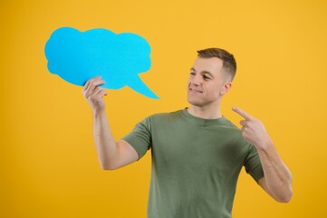 Cheerful young male pointing up and holding empty speech bubble with blank space for quote against vivid yellow background