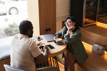 Portrait of two young people chatting at table during coffee break in graphic cafe interior, copy space