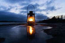 Vintage Oil Lantern Outdoors On The Ice Near The Sea. Old Kerosene Lamp Illuminates On The Sea Shore. Storm Clouds.