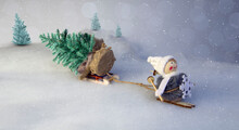 Toy Girl Snow Maiden, On Skis, Pulls A Forest Tree Behind Her Against The Background Of Lei In Out-of-focus And Bokeh And Falling Snow