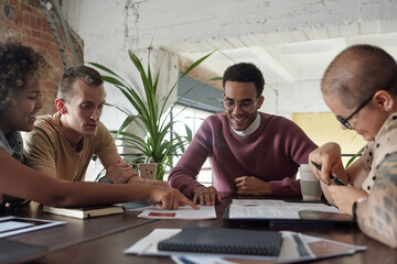 Poster - Happy young biracial businessman looking at financial paper while one of his colleagues pointing at it during discussion