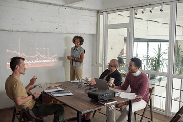 Poster - Group of young contemporary economists discussing rates during preentation while gathered by table in office