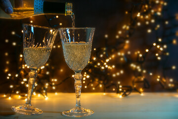 Two glasses are poured with champagne for a New Year party toast, golden bokeh lights in the dark background, copy space, selected focus