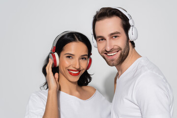 cheerful young couple in headphones looking at camera while listening music on grey.