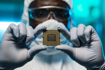 Poster - Gloved hands of African man in protective coveralls showing you microchip while holding it in front of camera
