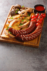 Canvas Print - Typical fast food Grilled sausages with potato wedges and mushrooms and sauce close-up on a wooden tray on the table. vertical