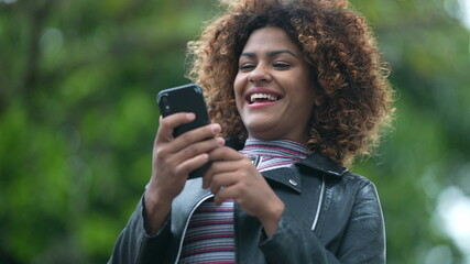 Surprised young Brazilian woman celebrating news notification on cellphone device outside