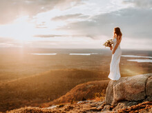 Bride Wedding Dress Standing On Edge Of Rock With Setting Sun