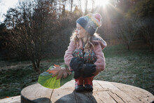 Girl Sat With Leaves In The Forest In Autumn At Sunset