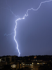 Wall Mural - vertical shot of a lightning strike behind a city at night